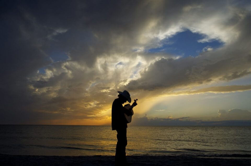 Waterfront silhouette of musician Clint Daniels playing guitar at sunset.